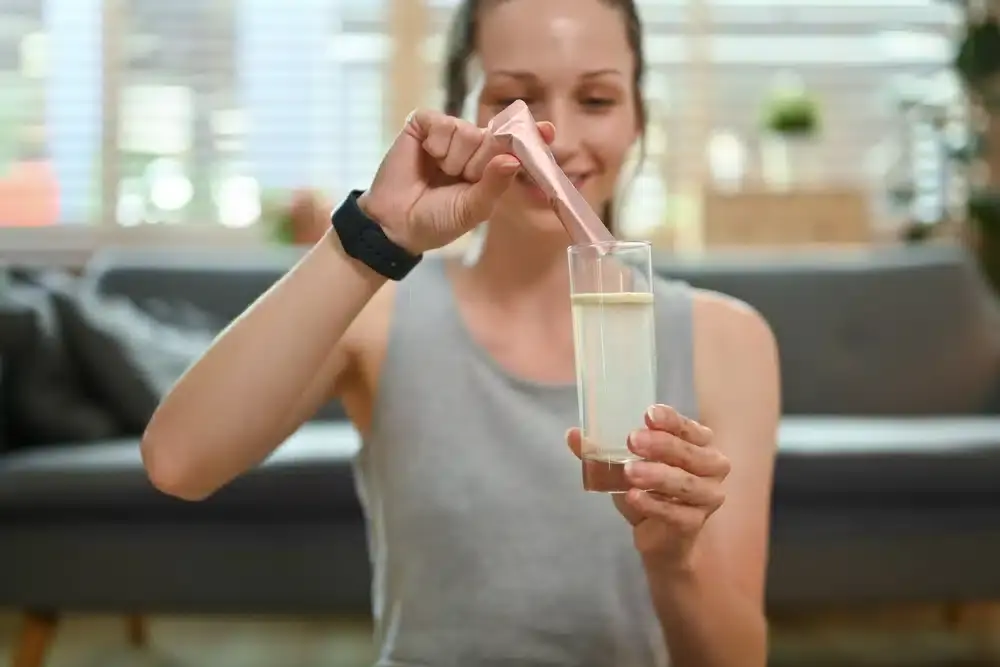 Sporty woman dissolving collagen powder in a glass of water.